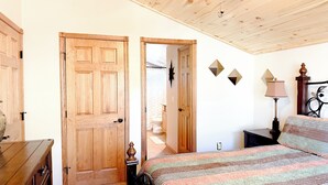 A bedroom with a wooden door, a bed with a striped blanket, a nightstand, a lamp, and a wall-mounted decoration. - Bela's in Torreon with Golf Membership (Show Low)