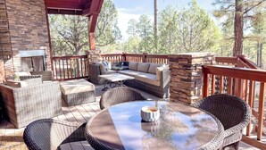 A covered outdoor seating area with wicker furniture, stone walls, and a view of trees. - Bela's in Torreon with Golf Membership (Show Low)