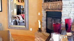 A living room with a stone fireplace, a flat-screen TV mounted above it, and a wooden coffee table with decorative items. - Bela's in Torreon with Golf Membership (Show Low)