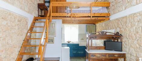 A rustic room with a wooden loft bed, a desk with a television, and a stone wall.