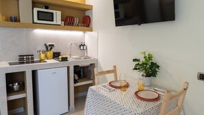 Une cuisine compacte équipée d’un four à micro-ondes, d’un évier et d’un petit réfrigérateur. On y trouve une table à manger avec des chaises et une plante en pot.