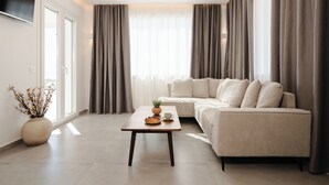 A modern living room with a sofa, a coffee table, a TV, and a large window with curtains. - Villa THÉA II, Villa THÉA Naxos (Vivlos)
