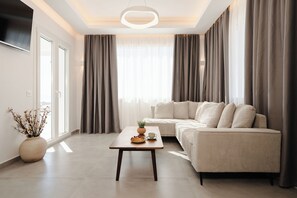 A modern living room with a sofa, a coffee table, a TV, and a large window with curtains. - Villa THÉA II, Villa THÉA Naxos (Vivlos)