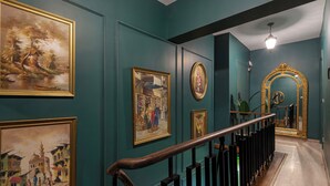 Un couloir aux murs de couleur turquoise, doté d’un plancher en bois et d’une rambarde noire. Plusieurs œuvres d’art encadrées ornent les murs.