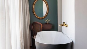Une salle de bain moderne avec une baignoire sur pieds, un miroir rond et une chaise en bois.
