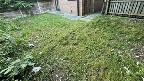Een achtertuin met een gazon, een bakstenen gebouw en een houten omheining.