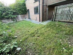 Ein Garten mit Rasenfläche, einem Ziegelgebäude und einem Holzzaun.