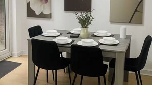 Een eetgedeelte met een houten tafel voor zes personen, omringd door zwarte stoelen. Boven de tafel hangen drie schilderijen van orchideeën aan de muur.