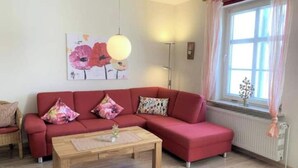 Un salon avec un canapé d’angle rouge, une table basse en bois et une grande fenêtre avec des rideaux.