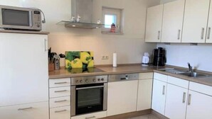 Une cuisine avec des meubles blancs, un four à micro-ondes, une cuisinière et une machine à café.