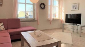 Un salon avec un canapé, une table basse, un téléviseur posé sur un meuble et une fenêtre avec des rideaux.