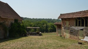 Ein rustikales Steinhaus mit einem Reetdach, einem Holztisch mit Stühlen und einem grünen Rasen.