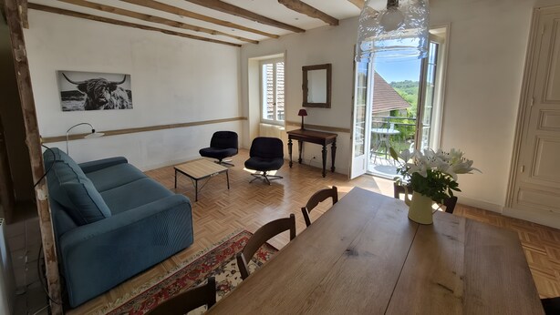 Ein Wohnzimmer mit einem blauen Sofa, einem Holzesstisch und Blick durch eine Glastür.