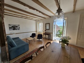 Een woonkamer met een blauwe bank, een houten eettafel en uitzicht door een glazen deur.