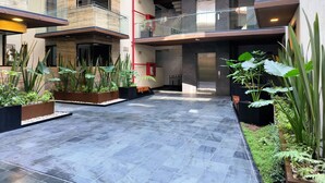 A modern building with multiple balconies, a central elevator, and various potted plants.
