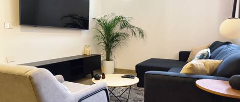 Una sala de estar moderna con un televisor de pantalla plana, un sofá, una mesita de centro y una planta en maceta.