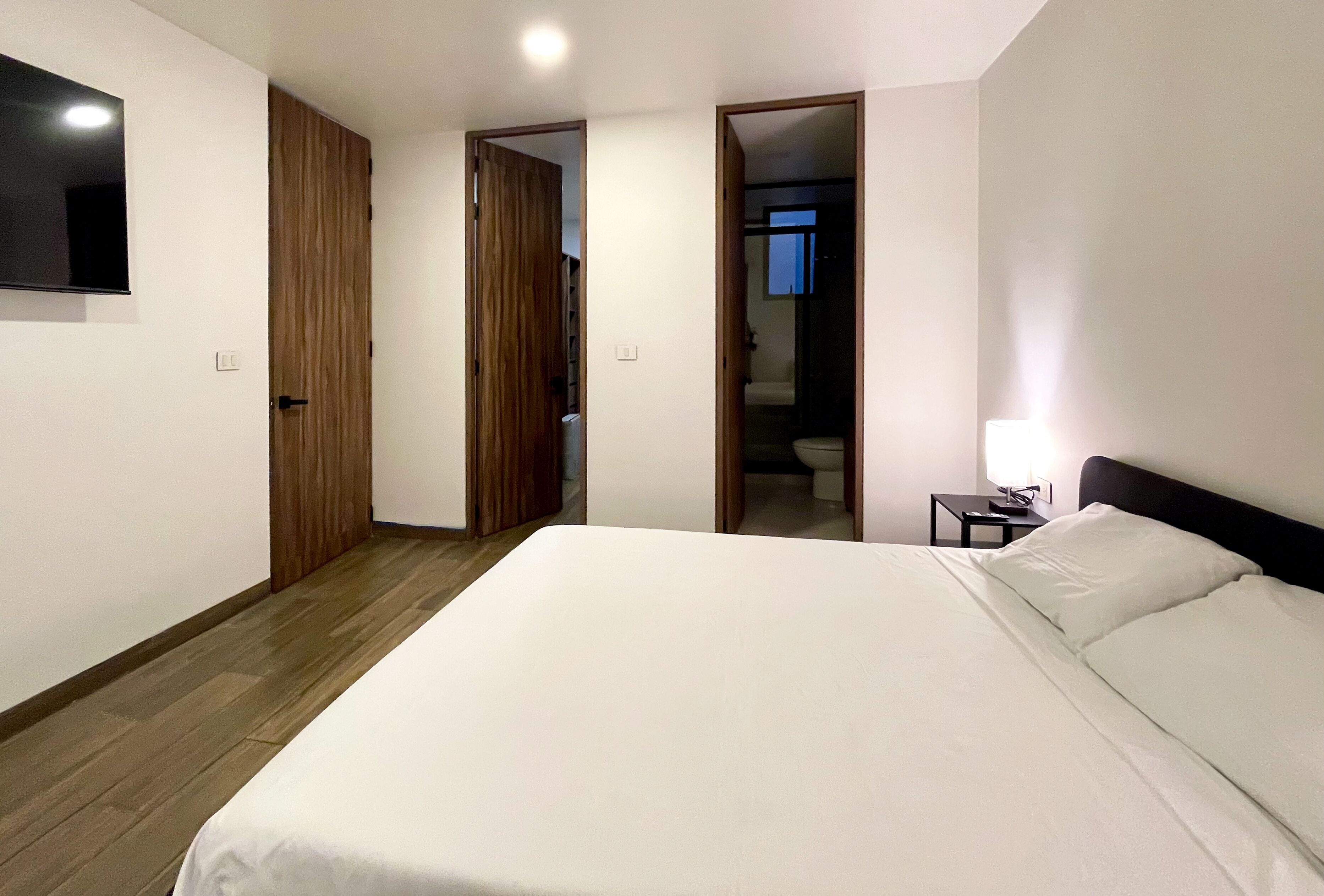 Une chambre à coucher avec un grand lit, une armoire en bois et une petite table de chevet avec une lampe.