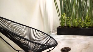 A modern interior with a black wireframe chair, a potted plant with long green leaves, and a tiled floor.