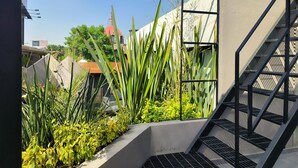 A rooftop garden with plants, a metal staircase, and a building in the background.