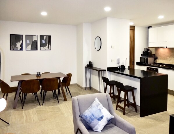 Un apartamento moderno con comedor, cocina con encimera negra y sala de estar con sofá gris.