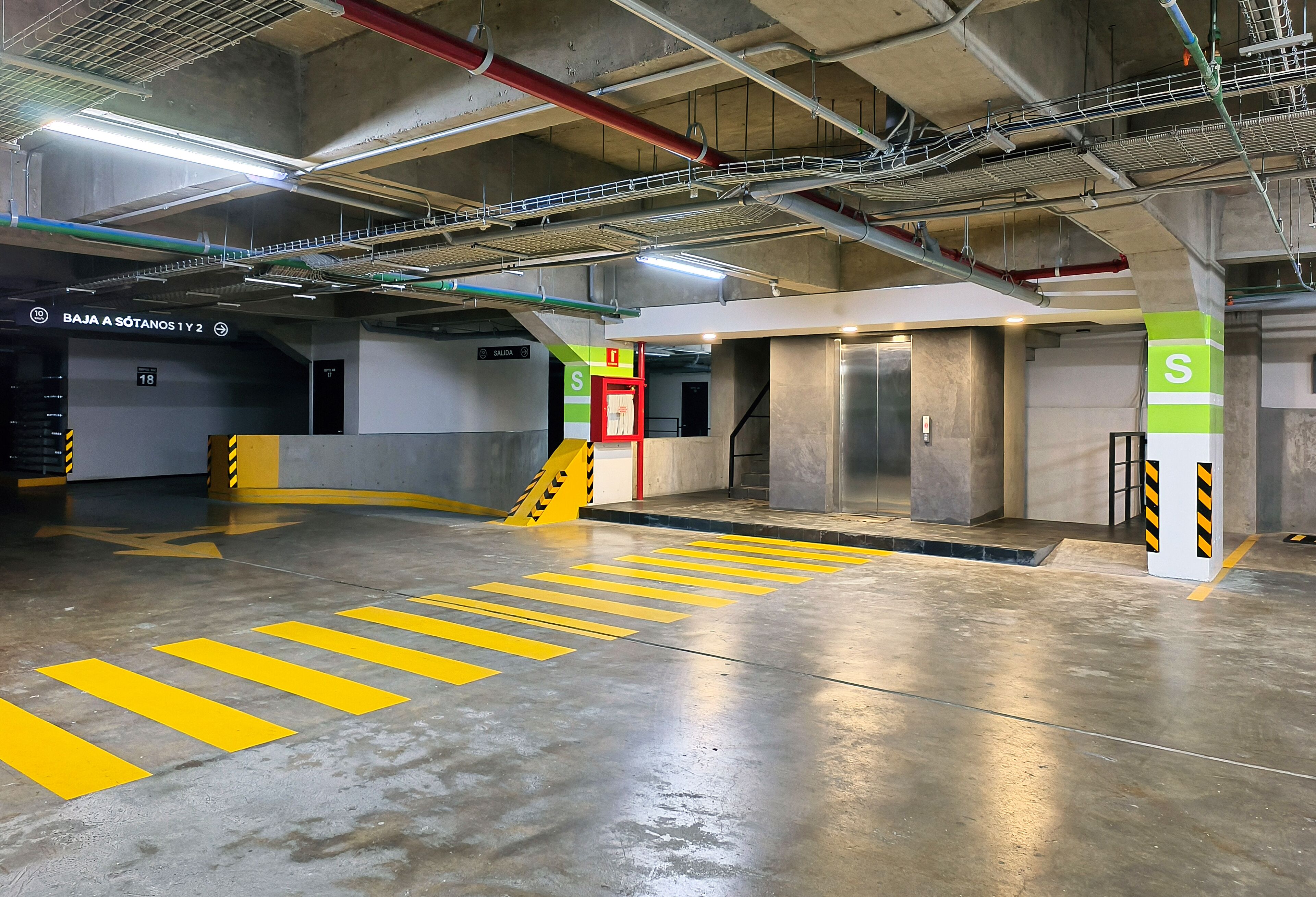An underground parking garage with concrete floors, yellow directional lines, and pillars marked with 'S'.
