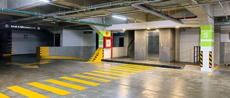 An underground parking garage with concrete floors, yellow directional lines, and pillars marked with 'S'.