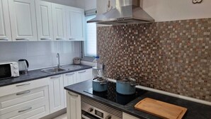 Eine moderne Küche mit weißen Schränken, einer schwarzen Arbeitsplatte, einer Edelstahl-Dunstabzugshaube, einer gefliesten Spritzschutzwand und einem Holzschnittbrett.