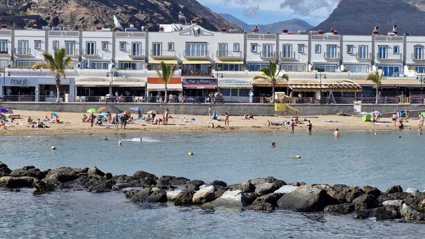 Ein Küstenhotel mit mehreren Balkonen, einem Sandstrand und Felsformationen im Wasser.