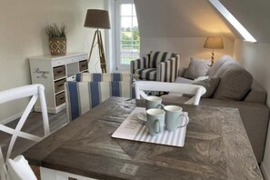 A cozy, well-lit room with a dining table, striped chairs, and a sofa. - Villa Seeperle - Seagull's Nest (Dahme)