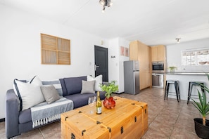 A modern living room with a sofa, a wooden coffee table, and a kitchen area with cabinets and appliances. - Big Bay Beach Club 182 (Cape Town)