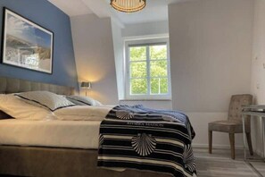 Ein Schlafzimmer mit einem Bett, einem Fenster, einem Stuhl und einem gerahmten Bild an der Wand.