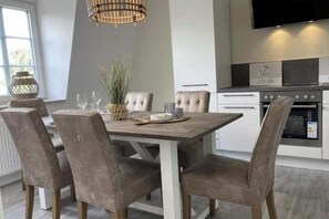 Eine moderne Küche mit einem Holzespeisetisch, vier gepolsterten Stühlen, einer Pendelleuchte und eingebauten Geräten.