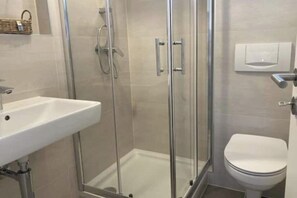 Ein Badezimmer mit einer Duschkabine, einem weißen Waschbecken und einer Toilette.