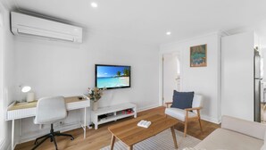 A modern living room with a flat-screen TV, a desk, a comfortable chair, and a small coffee table. - The Pearl by Book Jervis Bay A Fresh, Modern Family Retreat in Old Erowal Bay (Old Erowal Bay)
