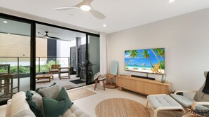 Een moderne woonkamer met een grote flatscreen-tv, een bank, een salontafel en een balkon met buitenmeubilair.