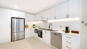 A modern kitchen with white cabinetry, stainless steel appliances, and a dishwasher. - Husky Beach Pad by Book Jervis Bay - Walk to the beach (Huskisson)