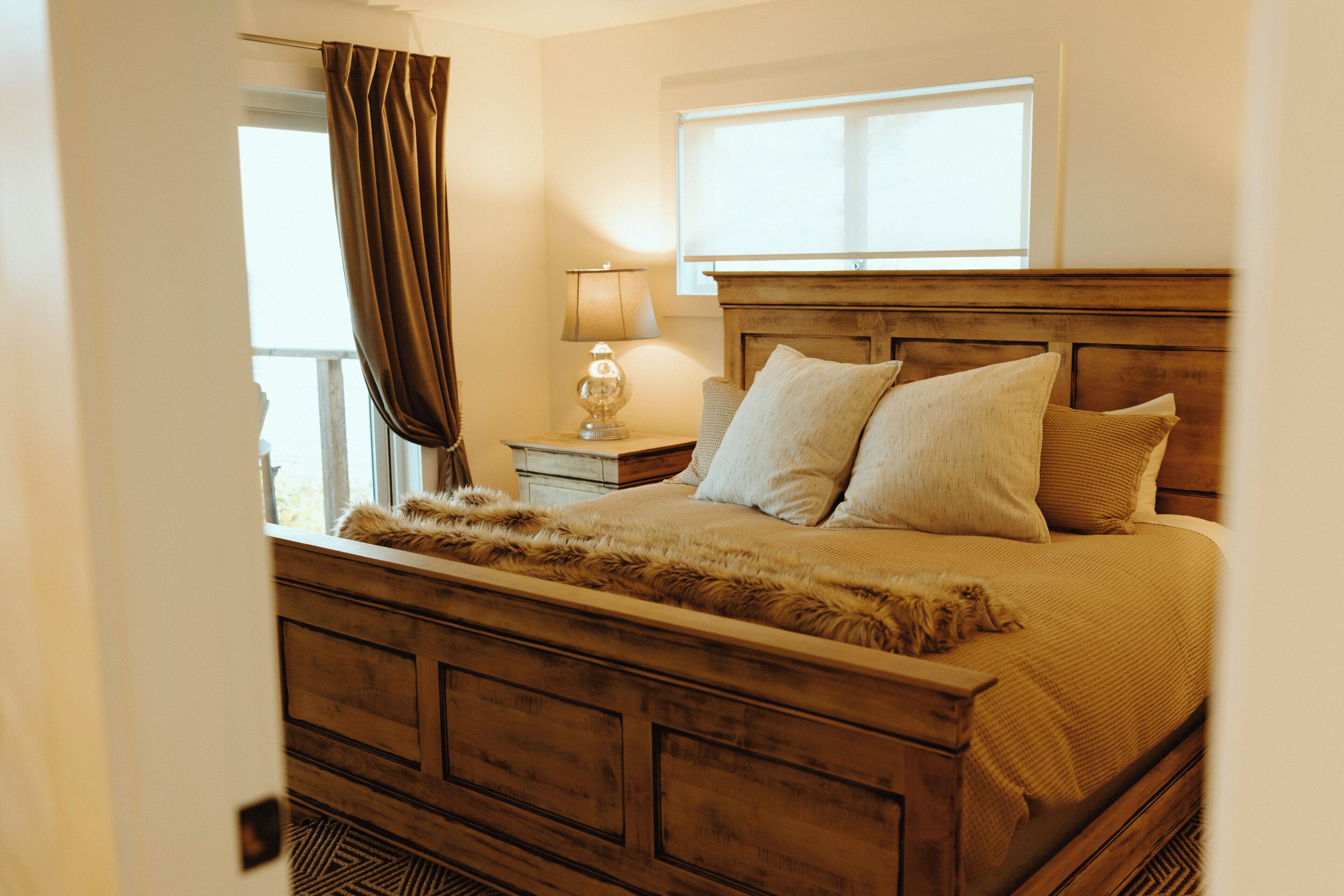 A bedroom with a wooden bed, a nightstand with a lamp, and a window with curtains.