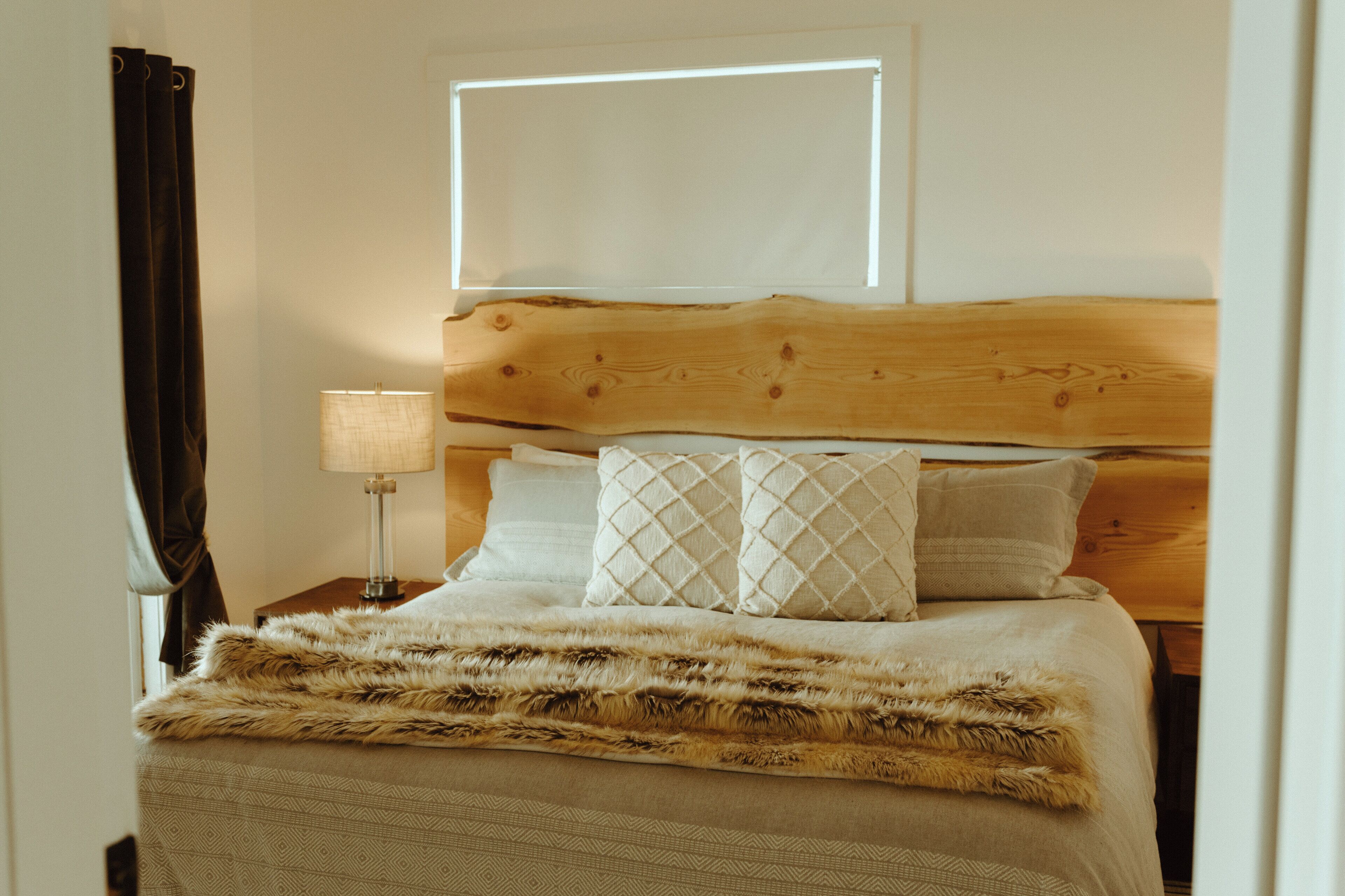 Une chambre à coucher avec une tête de lit en bois, un plaid en fausse fourrure et une lampe de chevet.