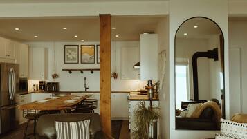 Une cuisine moderne avec des meubles blancs, une table à manger en bois et un îlot central. On y trouve également un espace salon avec un canapé en cuir et un grand miroir.