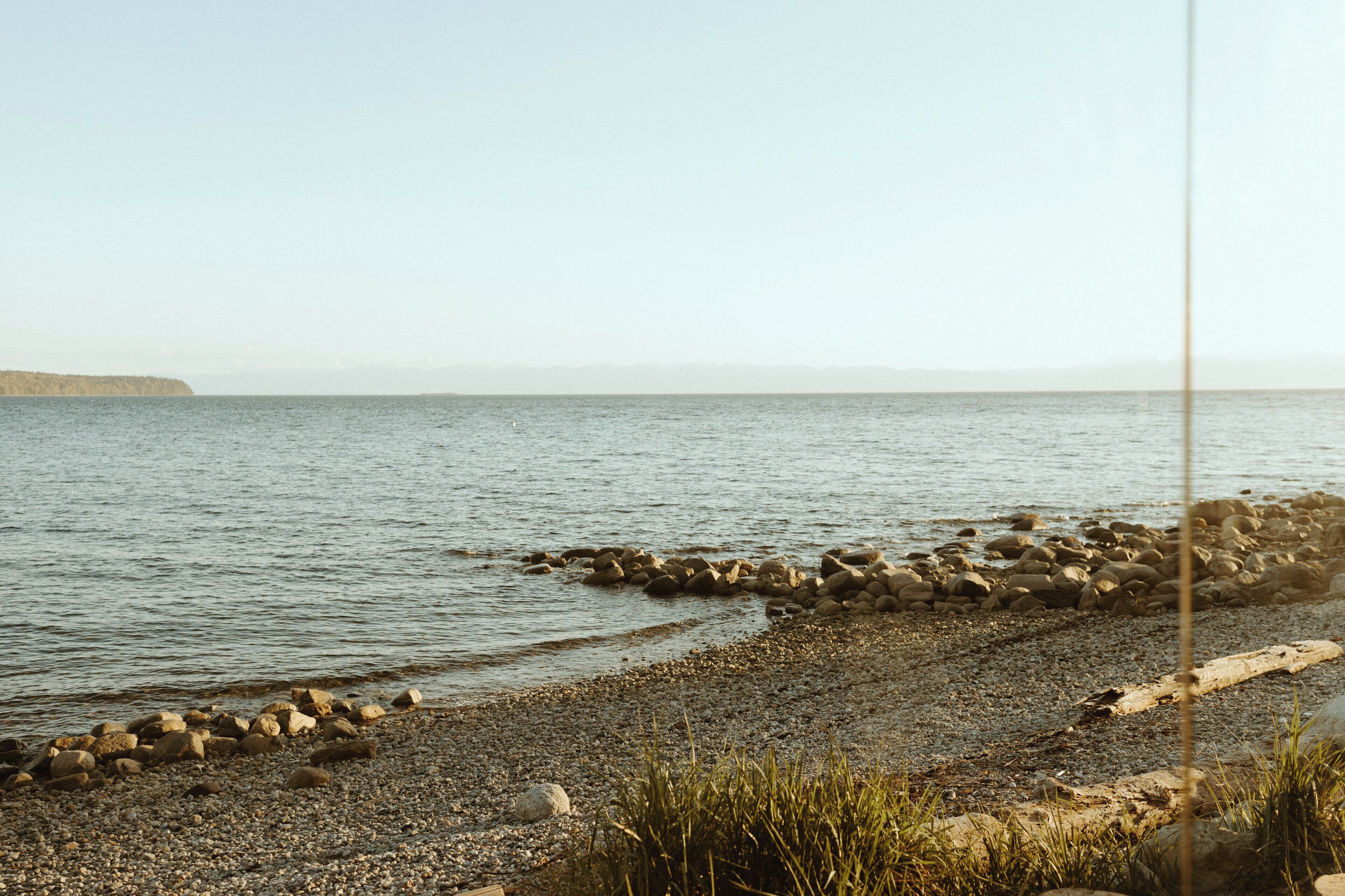 A rocky shoreline with calm water and distant landforms.