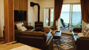 Ein Wohnzimmer mit Kamin, Ledersofas, einem Flachbildfernseher und Meerblick durch große Fenster.