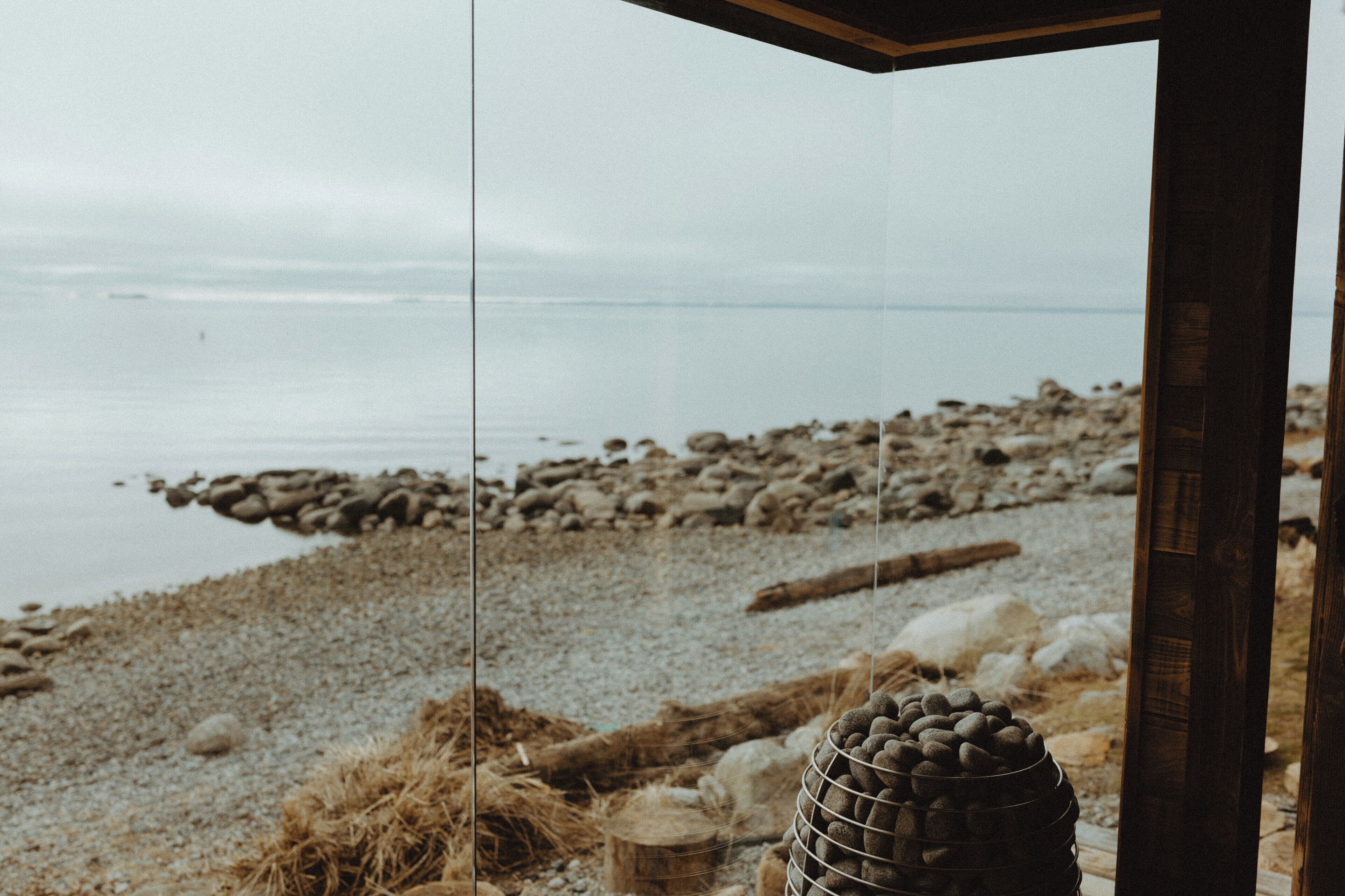 A view through a glass door of a beachside location with a rocky shoreline and calm water.