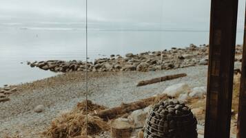 A view through a glass door of a beachside location with a rocky shoreline and calm water.