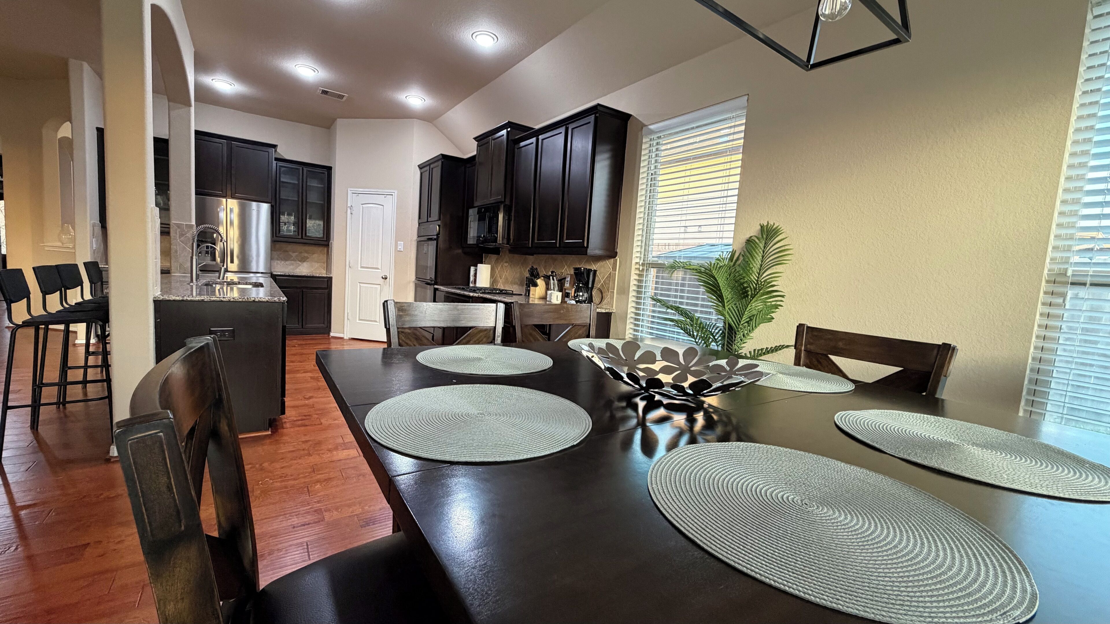A modern kitchen with dark cabinetry, a central island, and a dining area with a long table and chairs.