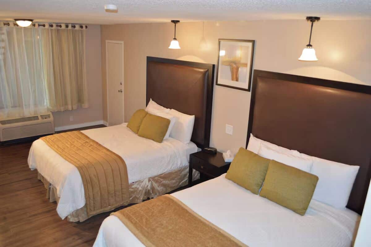 A hotel room with two beds, each with a headboard, a bedside table, and a lamp.