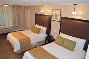 Ein Hotelzimmer mit zwei Betten, jeweils mit Kopfteil, Nachttisch und Lampe.