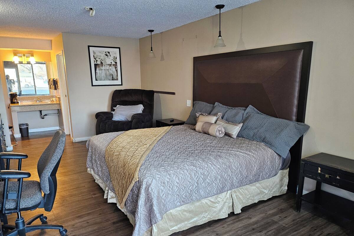 A bedroom with a large bed, a chair, a desk, and a mirror.