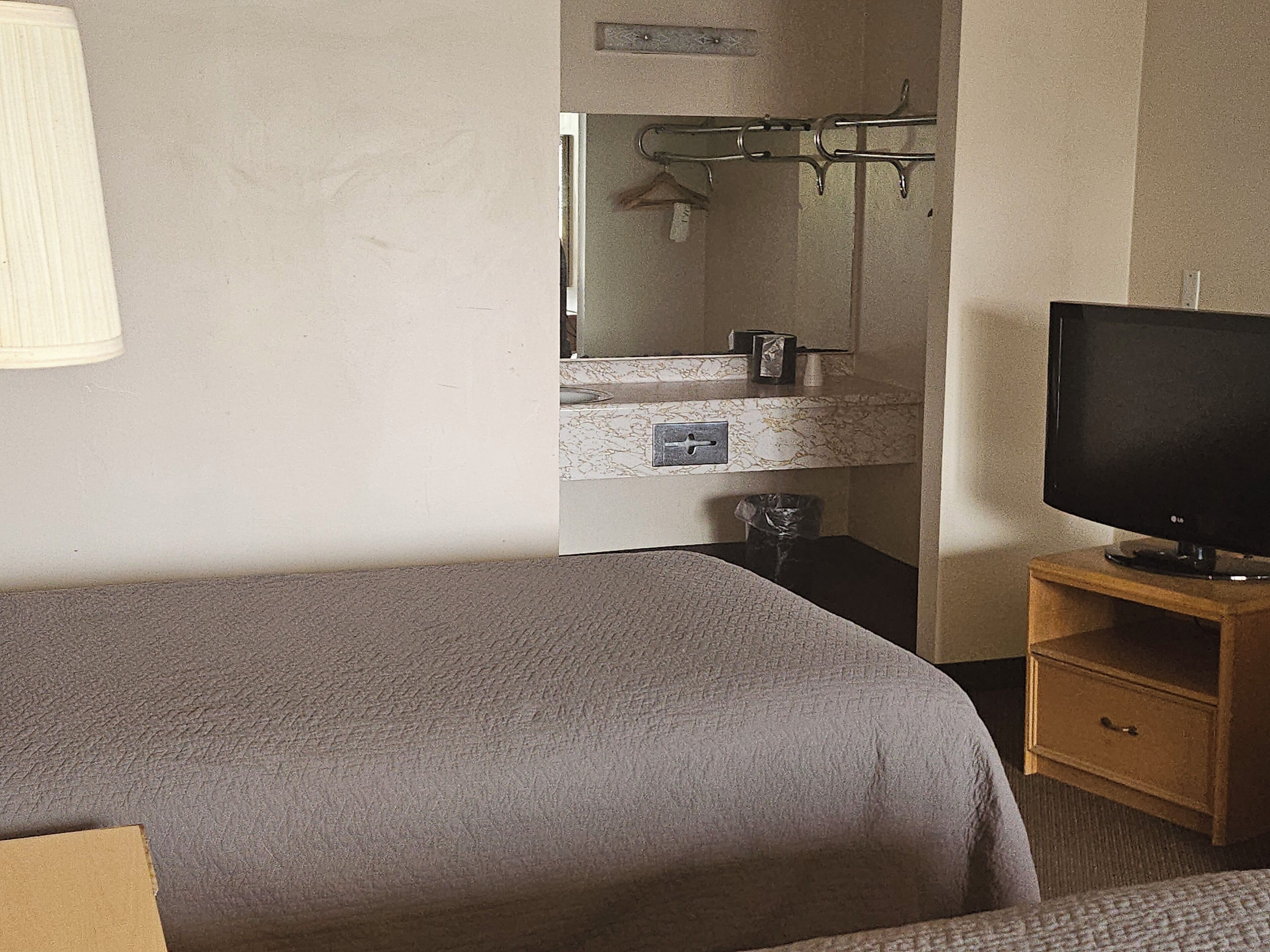 Una camera da letto con un letto, una TV su un mobile in legno, un bagno con uno specchio e un portaservizi.
