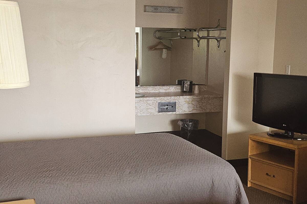 A bedroom with a bed, a TV on a wooden stand, a bathroom with a mirror, and a towel rack.