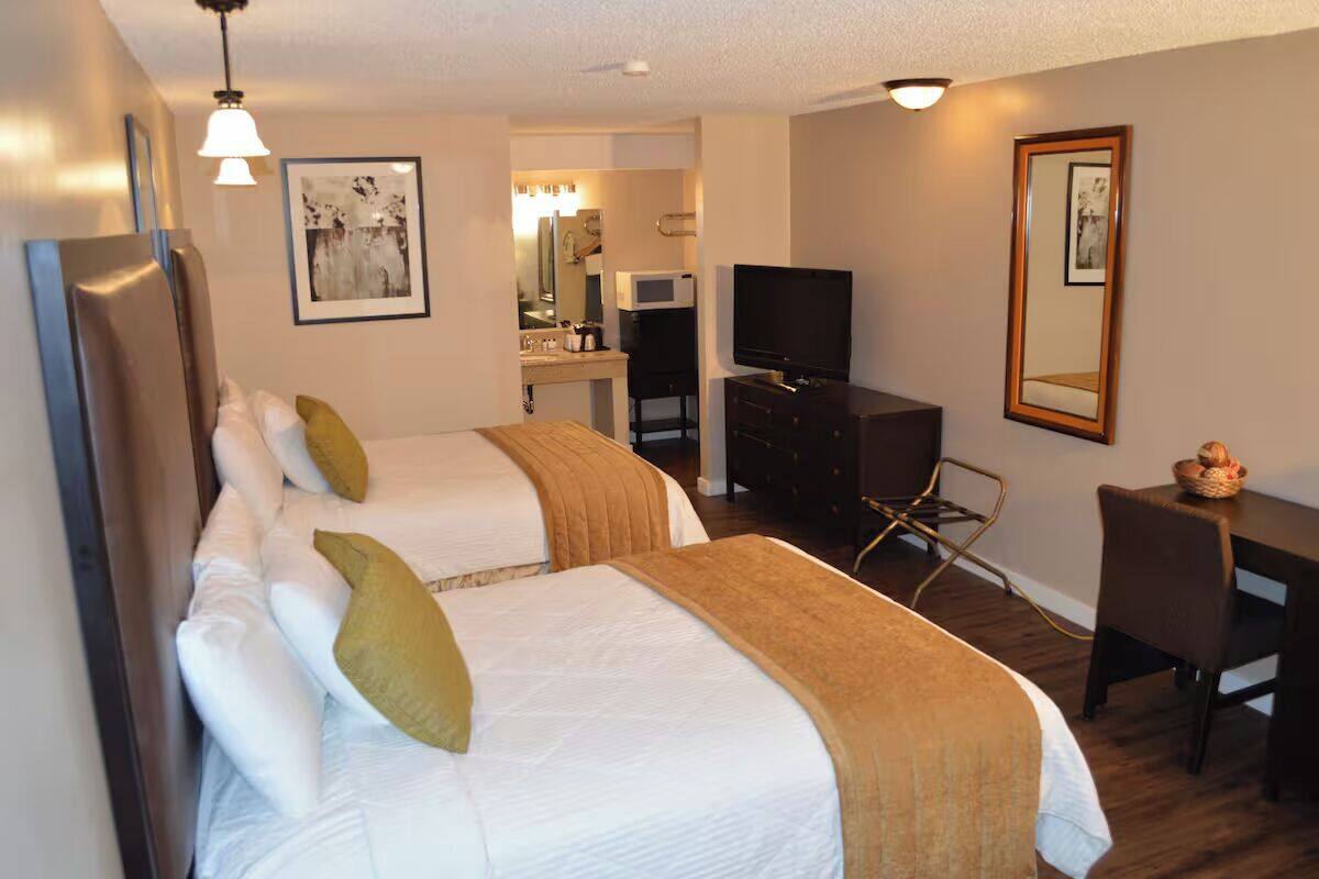 A hotel room with two beds, a desk, a chair, a television, and a bathroom visible through an open door.